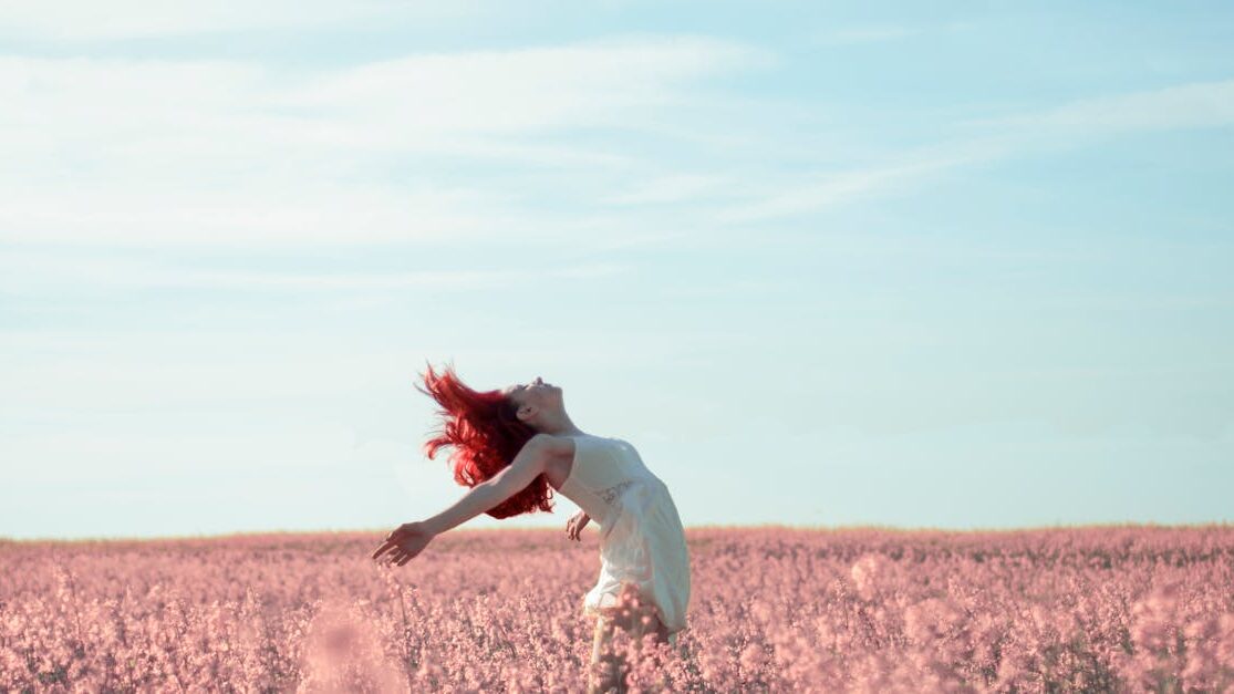 pexels-photo-1146242-1146242 Woman with red hair in a white dress expressing freedom in a vibrant summer field.