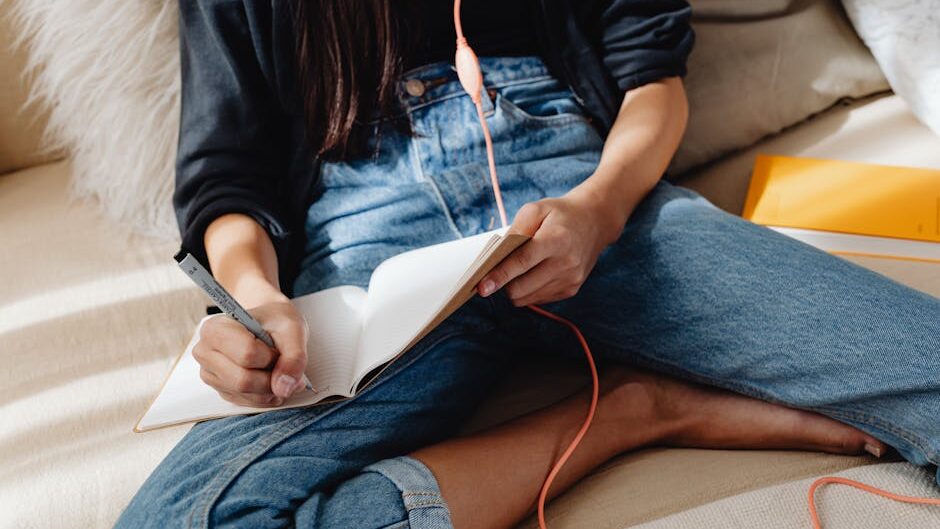 pexels-photo-7283634-7283634 A young woman sits on a cozy couch, writing in a notebook, with earphones in. Casual and relaxed setting.